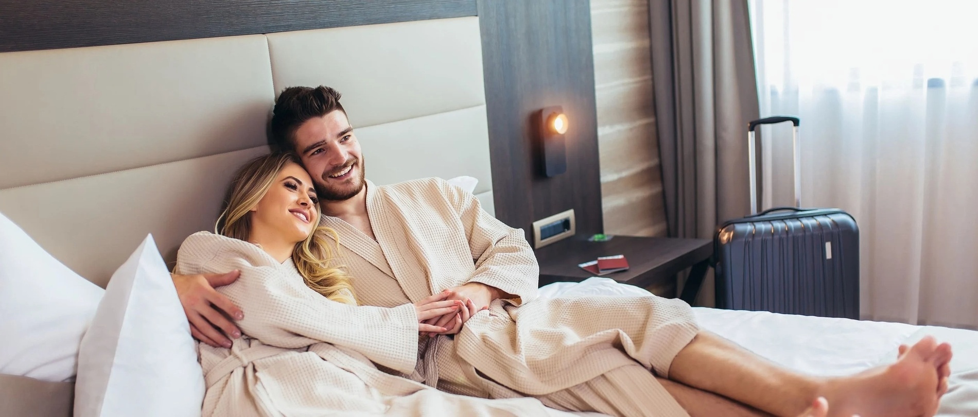 um homem e uma mulher estão deitados em uma cama com uma mala ao lado deles