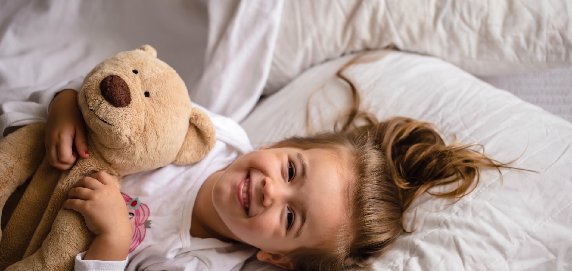 a little girl laying in bed holding a teddy bear
