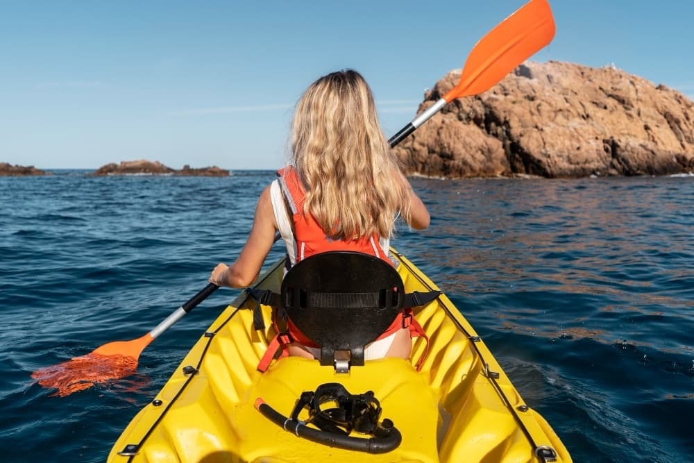 a woman in a yellow kayak with an orange paddle