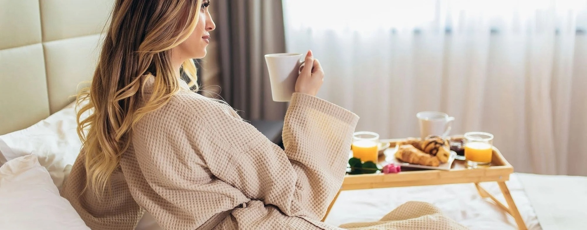 uma mulher está sentada em uma cama com uma bandeja de café e croissants