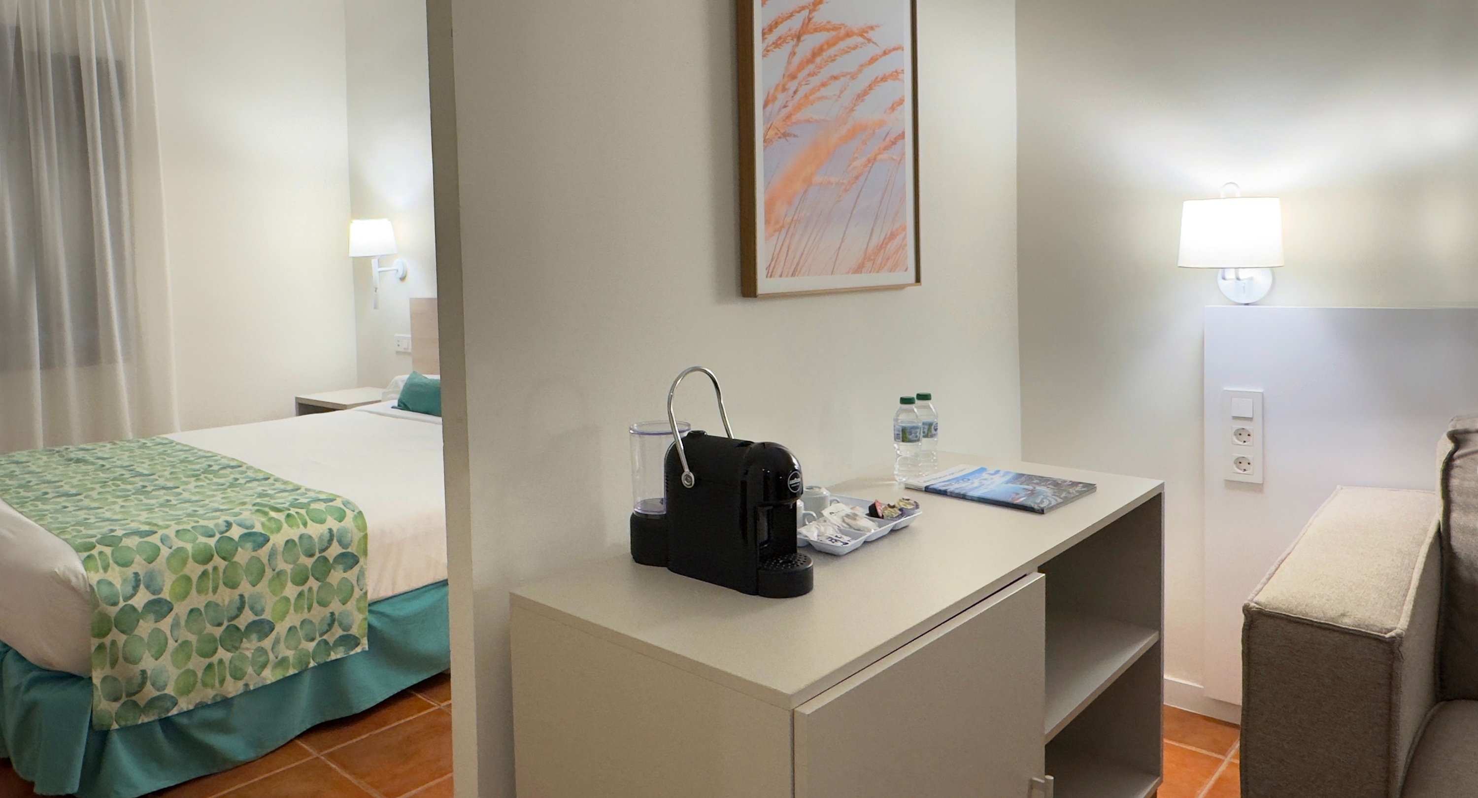 Habitación Dynastic Corporativa: Cama, cafetera Nespresso, botellas de agua y cuadro decorativo.