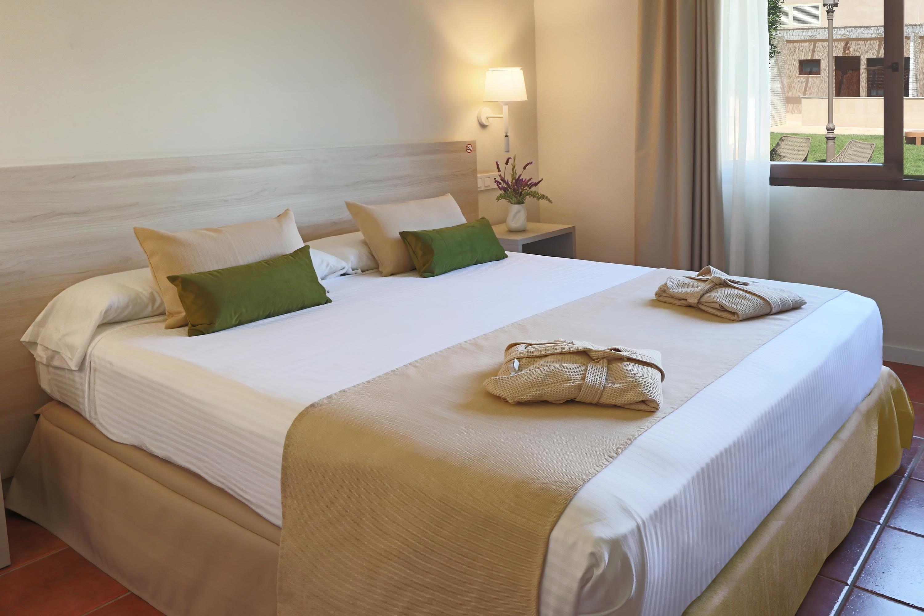 Cama confortable con manta gris y almohadas, luces de lectura. Estilo Dynastic Corporativa.