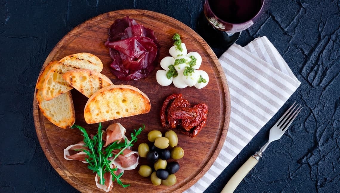 uma tábua de madeira cheia de comida e um copo de vinho