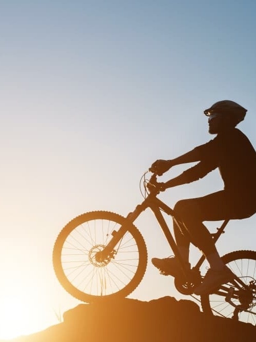 a man is riding a bike on top of a hill at sunset .
