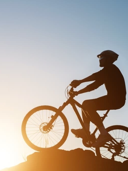 um homem está andando de bicicleta em uma colina ao pôr do sol .