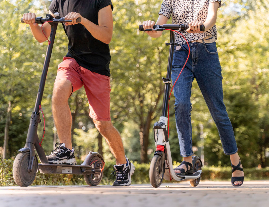 Casal se diverte em patinetes elétricos em um parque ensolarado, ideal para Dynastic Resorts e lazer.
