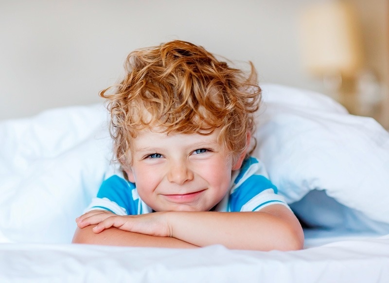 a young boy with curly hair is smiling while laying under a blanket
