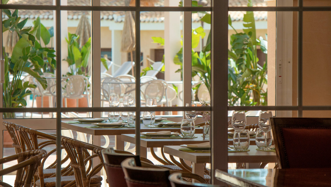 Comedor de hotel Dynastic Resorts con vistas al jardín y terraza, mesas puestas y ambiente luminoso.