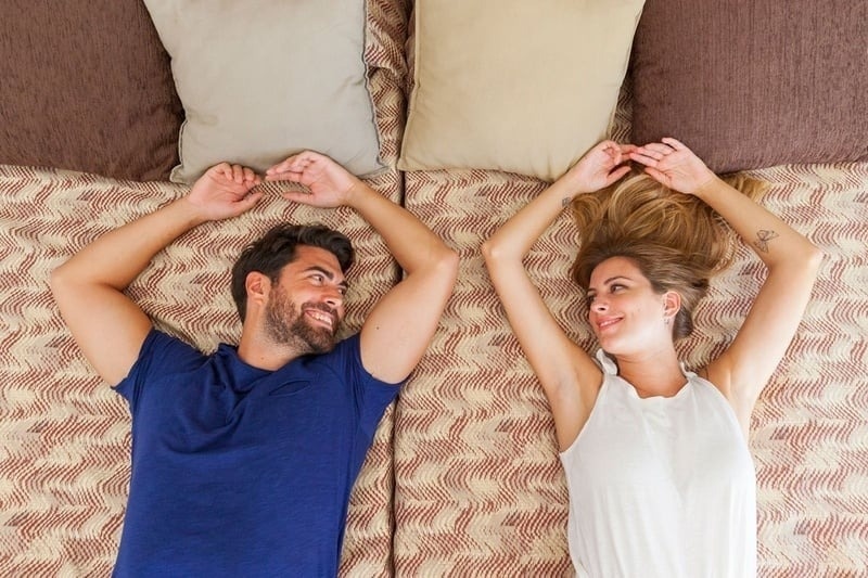 a man and a woman are laying on a bed with their arms outstretched