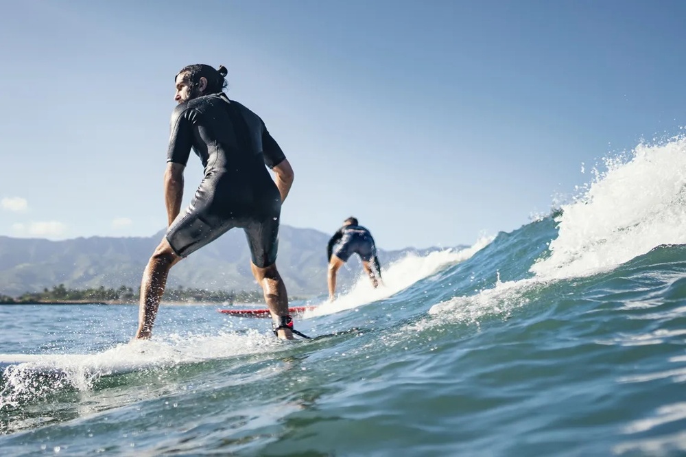 dos hombres surfeando en el océano uno de ellos con traje de neopreno
