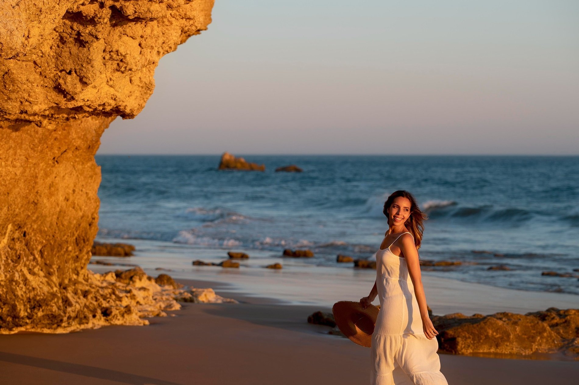 eine Frau in einem weißen Kleid steht am Strand