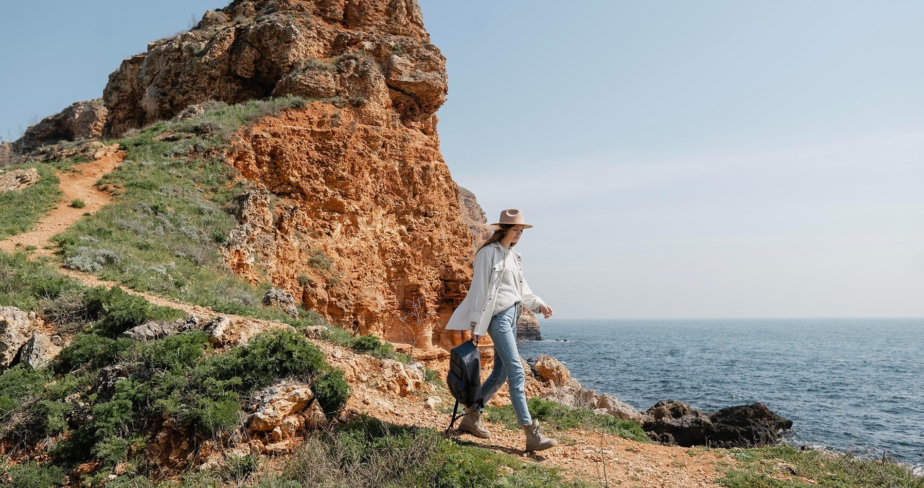 Eine Frau steht auf einem Felsen mit einem Rucksack und schaut auf das Meer