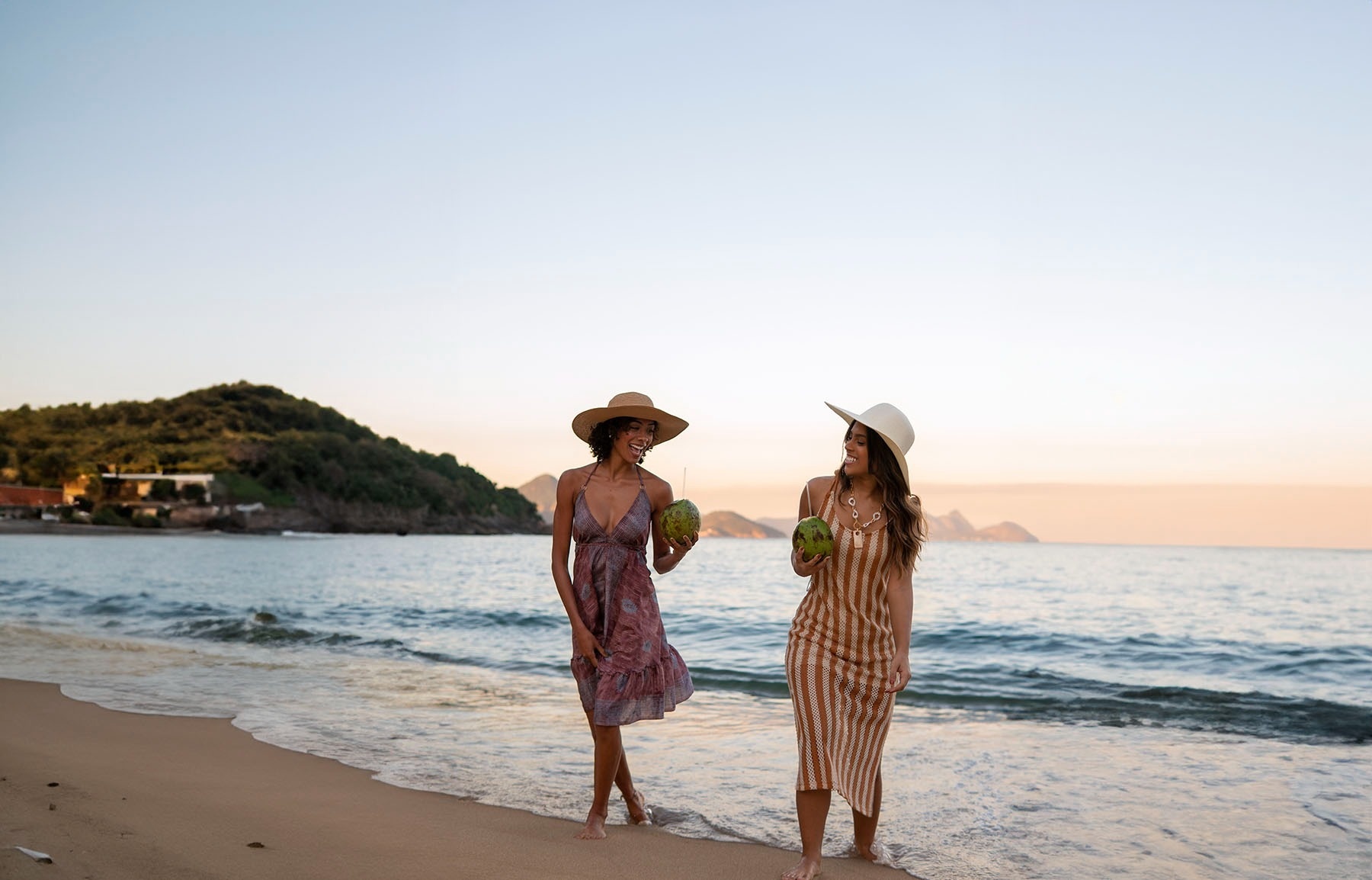 dos mujeres caminan por la playa con cocos en sus manos