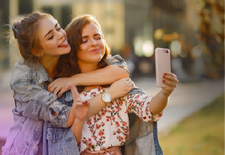 two girls are hugging and taking a selfie with a cell phone