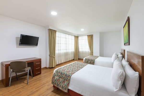 a hotel room with two beds a desk and a flat screen tv