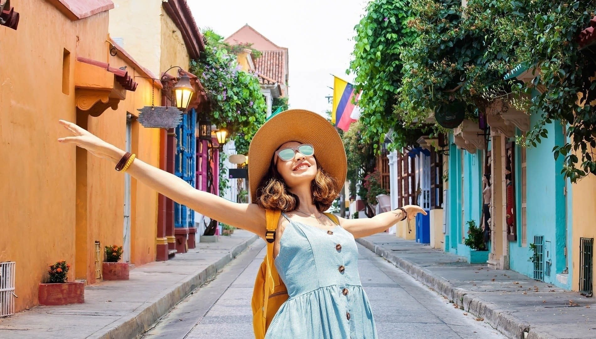 una mujer con sombrero y mochila camina por una calle colorida