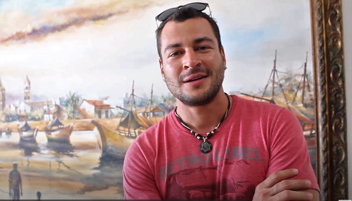 um homem com uma camisa vermelha e um colar com a letra t em frente a uma pintura