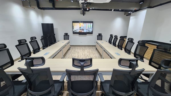 una sala de conferencias con mesas y sillas y una pantalla en la pared