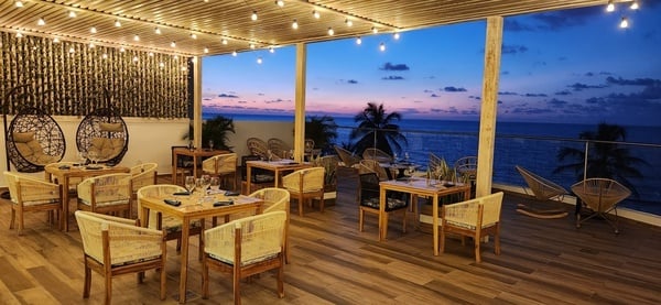 una terraza con mesas y sillas con vistas al océano al atardecer
