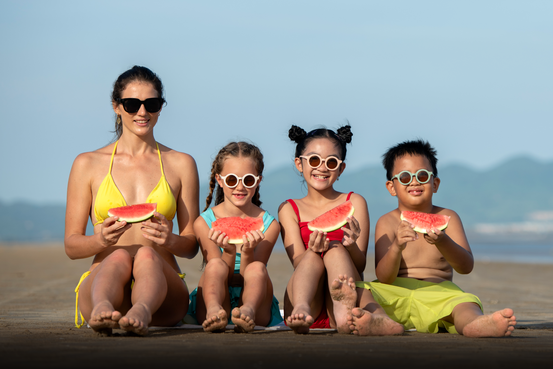 una mujer y tres niños comiendo sandía en la playa