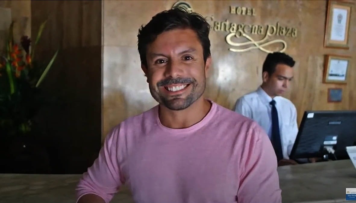 um homem em uma camisa rosa está sorrindo na recepção de um hotel