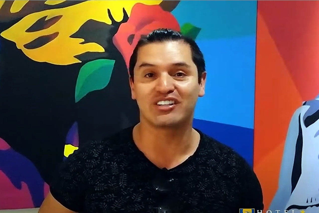 um homem com uma camisa preta está em frente a uma pintura colorida