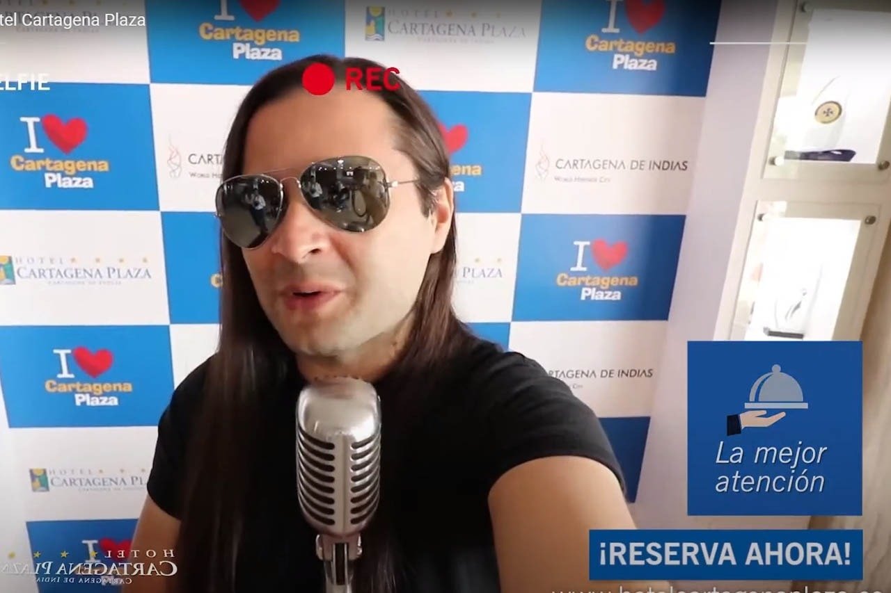 un hombre con gafas de sol y un micrófono frente a un fondo que dice cartagena plaza