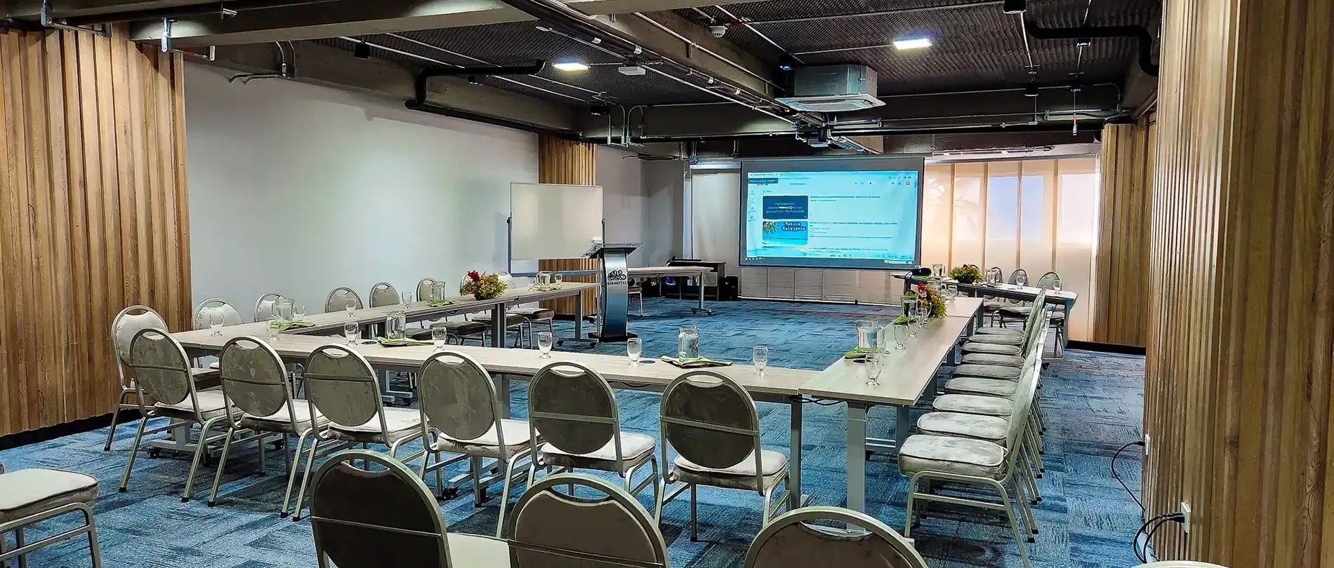 una sala de conferencias con mesas y sillas y una pantalla de proyección
