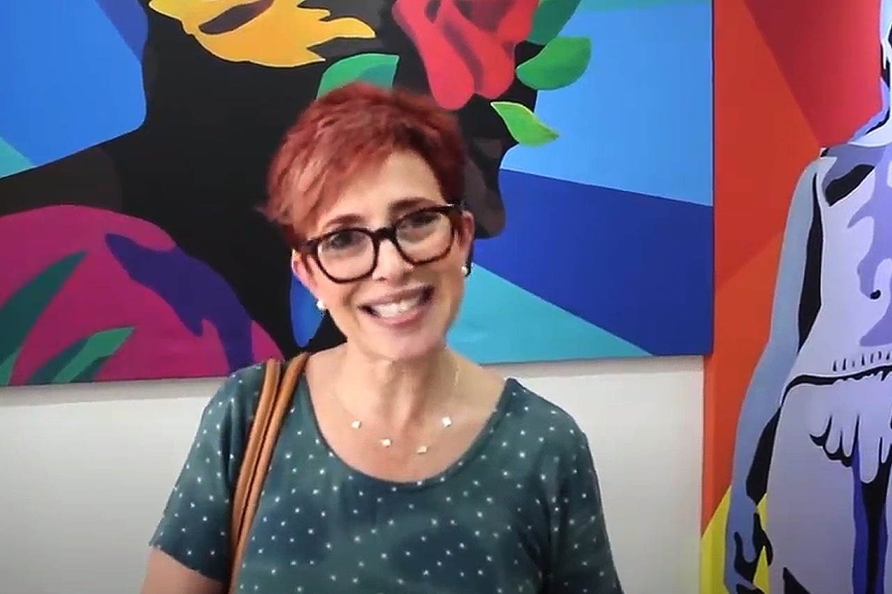 uma mulher de óculos está sorrindo na frente de uma pintura colorida