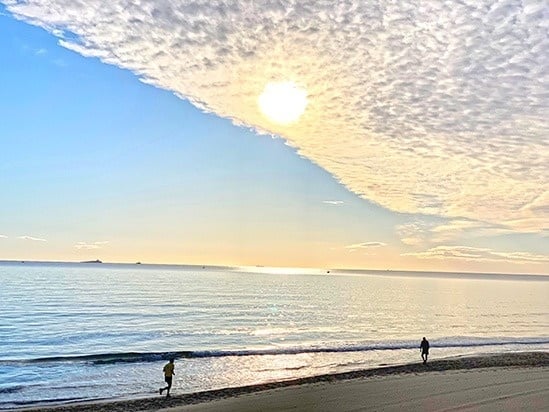 a person walking on the beach at sunset with the sun shining through the clouds