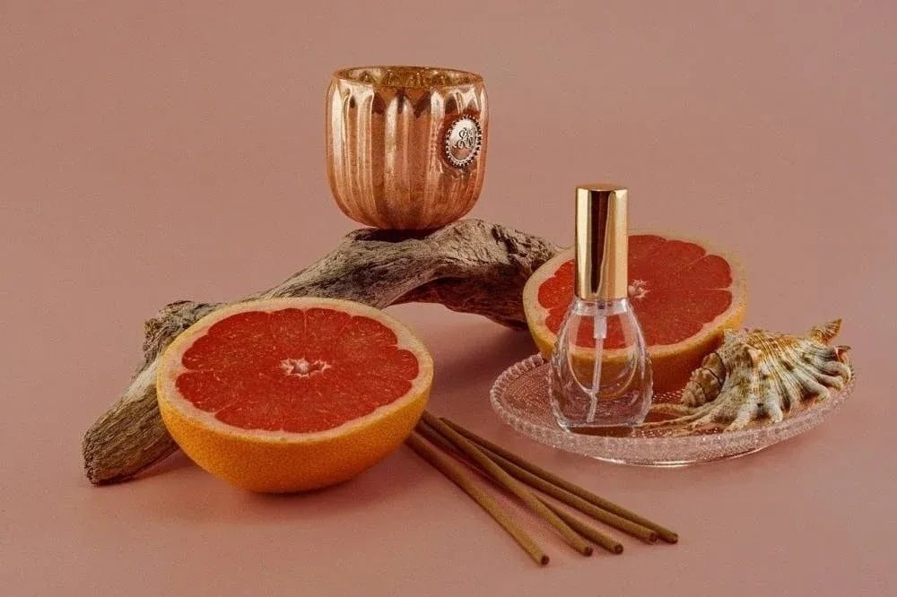 a grapefruit , a bottle of perfume , incense sticks , and a shell on a plate .