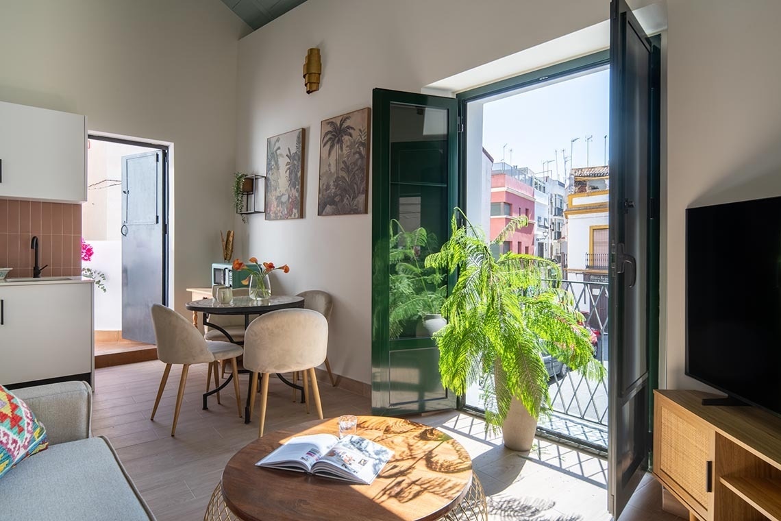 Un luminoso salón-comedor con cocina integrada y balcón se abre a una colorida calle urbana.