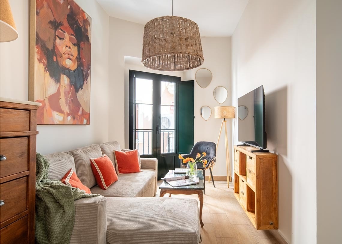 Un salón acogedor y luminoso con un sofá chaise longue, un cuadro grande, muebles de madera y toques naturales.