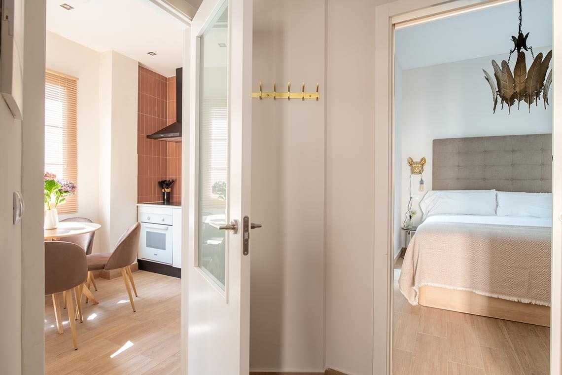 Un interior luminoso presenta un pasillo que enlaza una cocina con azulejos terracota y un dormitorio con una cama confortable.