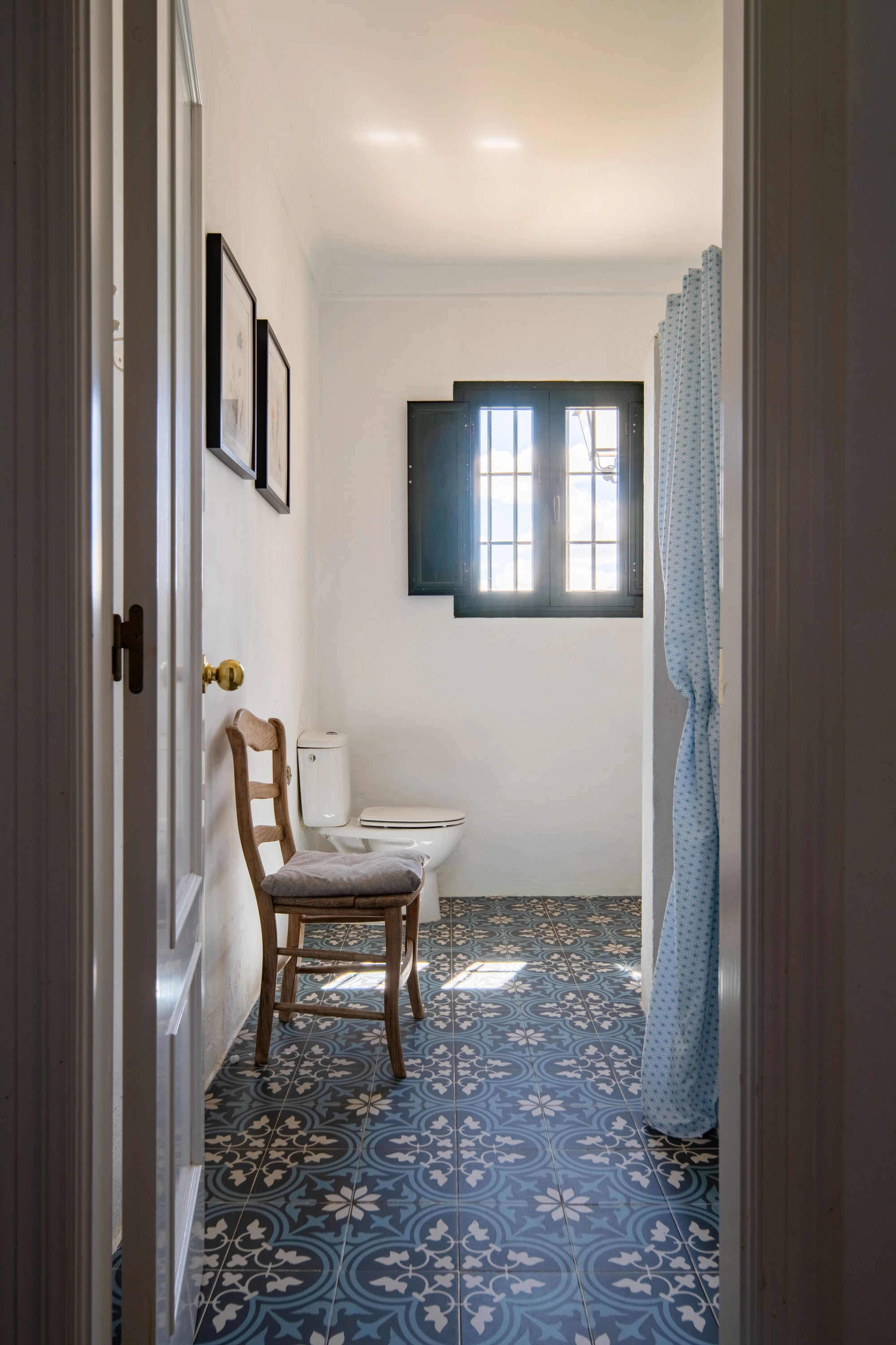 Bathroom with blue patterned tiles, toilet, chair, and window. Epoca Suites: Corporativa