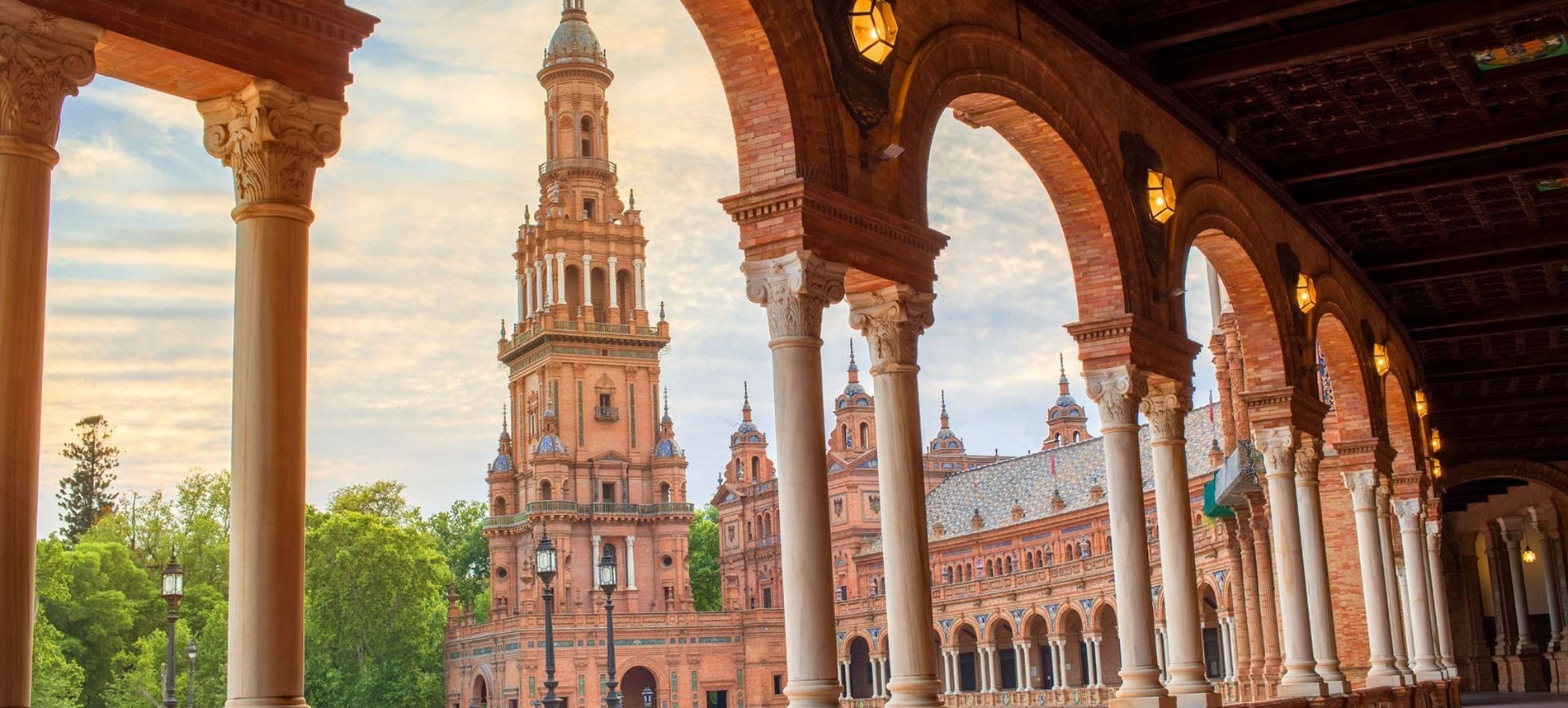 Una gran construcción con una torre central se asoma por debajo de una arcada de columnas y arcos de ladrillo.