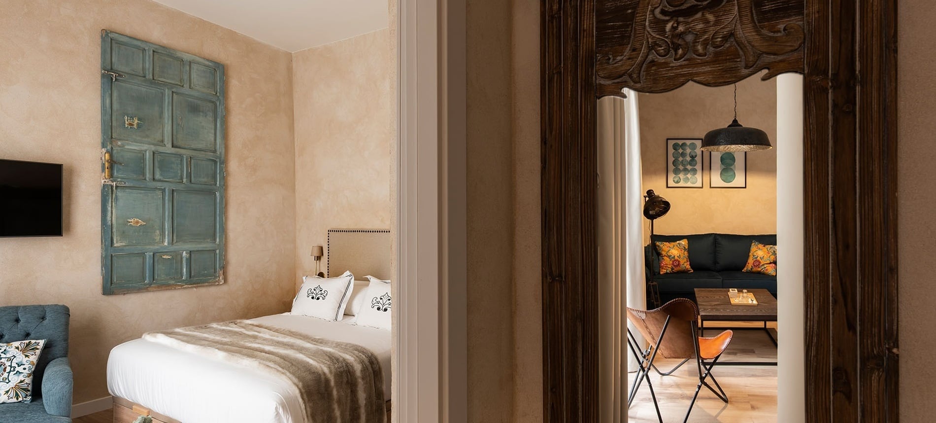 La imagen muestra dos habitaciones, un dormitorio con una puerta decorativa azul y una sala de estar con un sofá y una silla de mariposa, conectadas por un umbral de madera tallada.