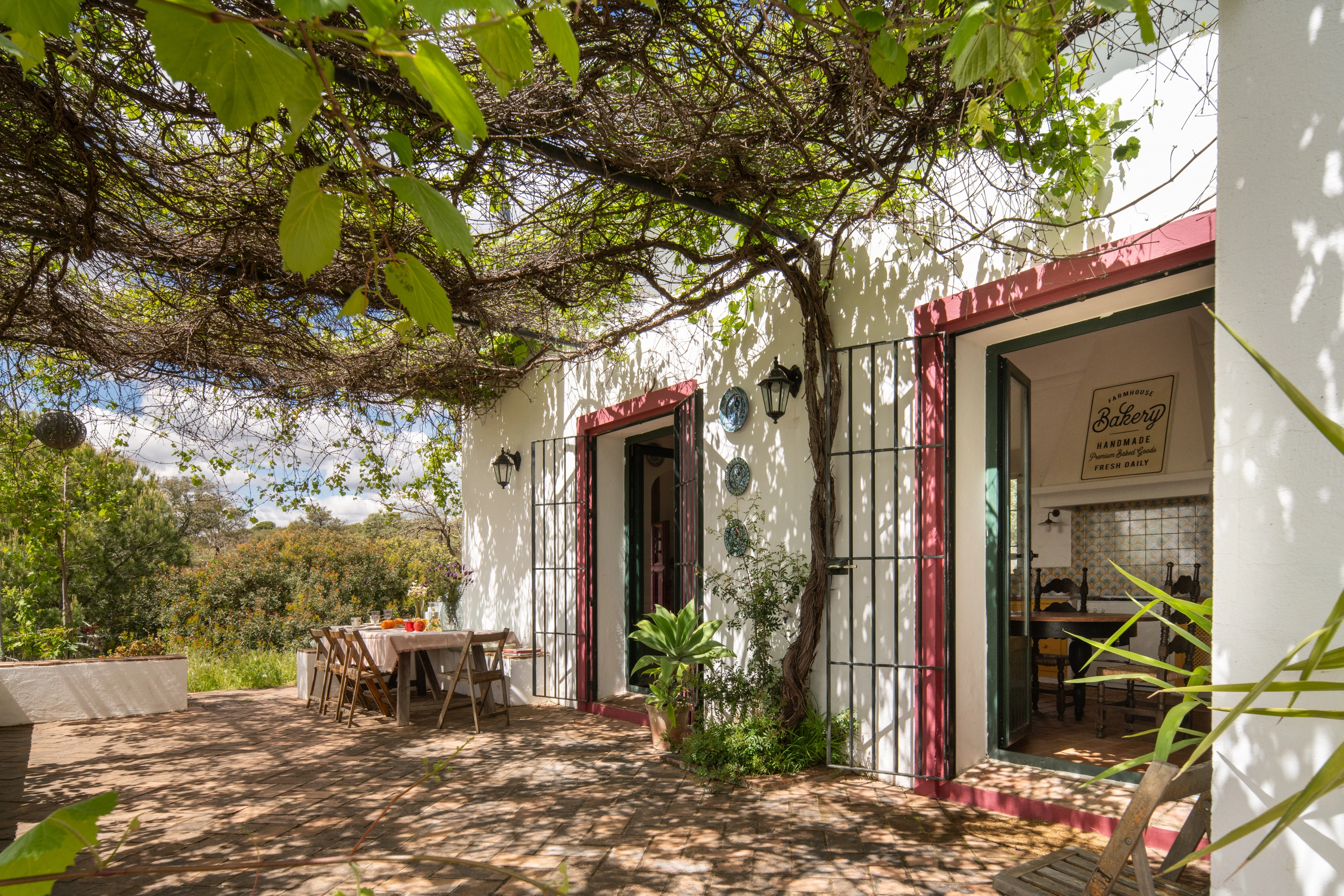 Outdoor dining area with vineyard Epoca Suites: Corporativa, table set for meals, and bakery sign visible inside.