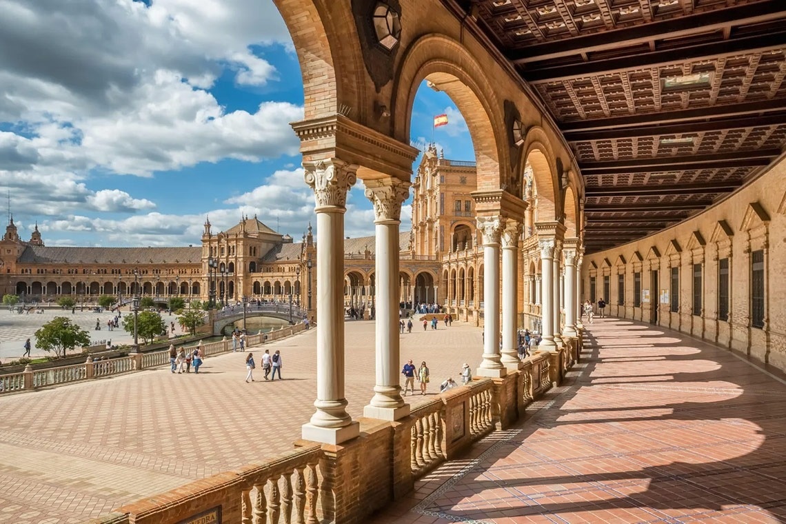 un grupo de personas camina por un largo corredor con columnas y un edificio en el fondo