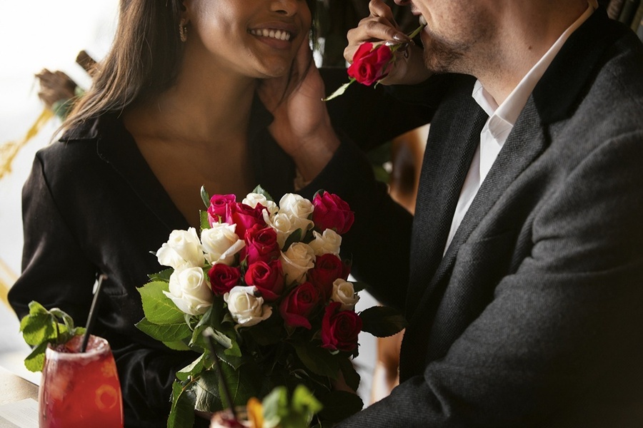 un hombre besa una rosa a una mujer que sostiene un ramo de rosas