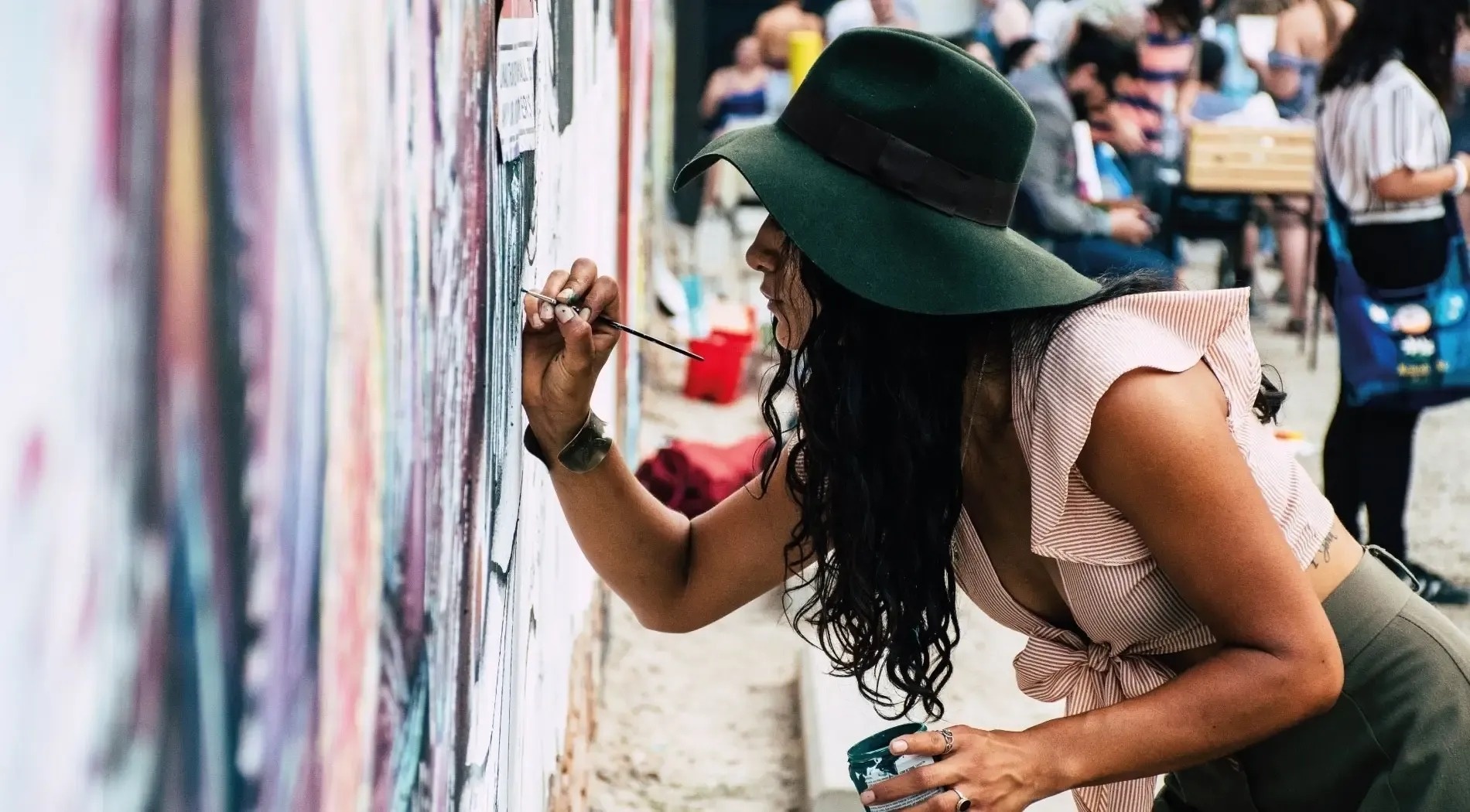a woman wearing a green hat is painting on a wall