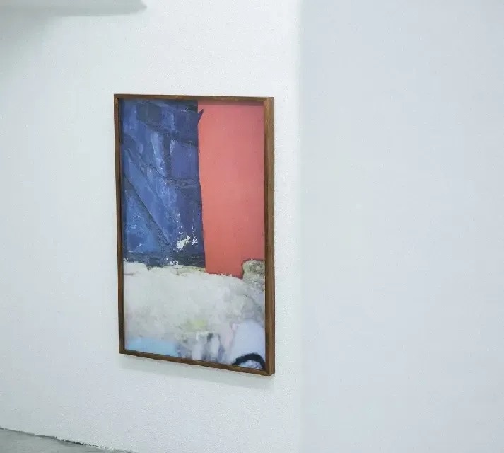 a large painting in a wooden frame is hanging on a white wall .