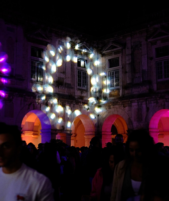 a group of people are standing in front of a building with lights projected on it