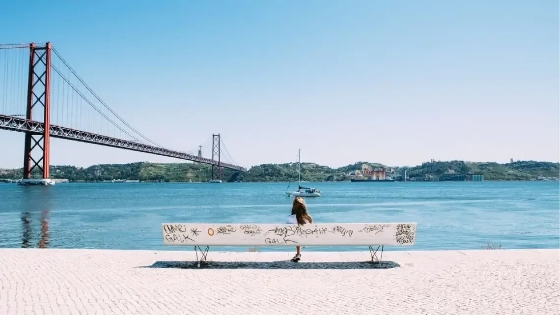 a woman sits on a bench with graffiti on it in front of a bridge