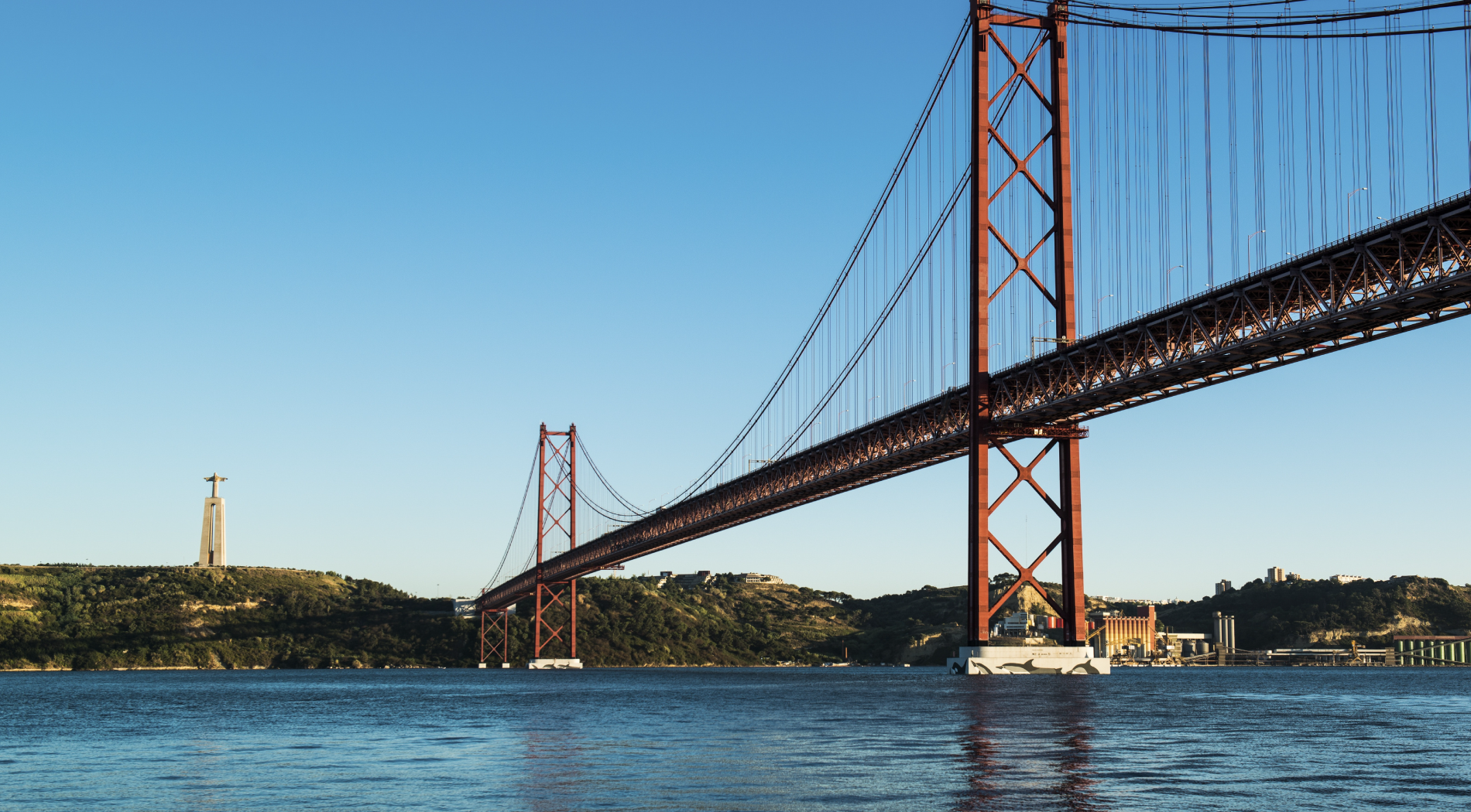 un puente rojo sobre un río con una estatua en la colina al fondo