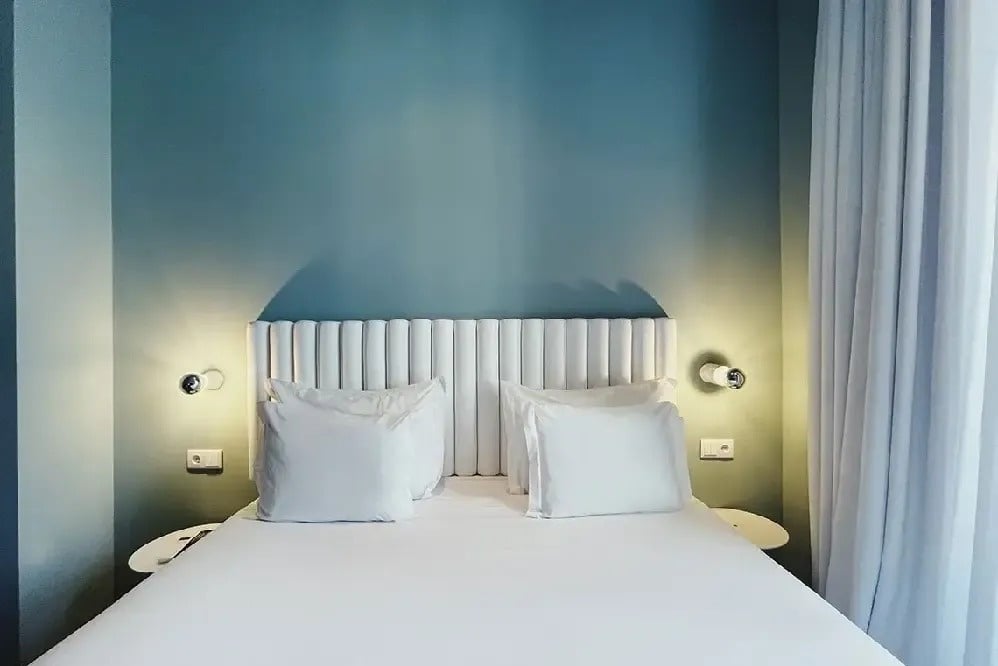 a bed with white sheets and pillows in front of a blue wall