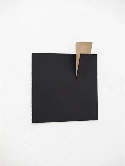 una pintura cuadrada negra con una pieza de madera en la esquina está colgada en una pared blanca .