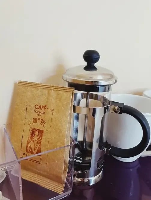 a bag of cafe torrado sits next to a french press