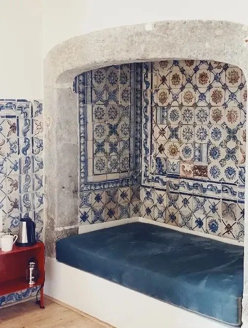 a bed in a corner of a room with blue and white tiles