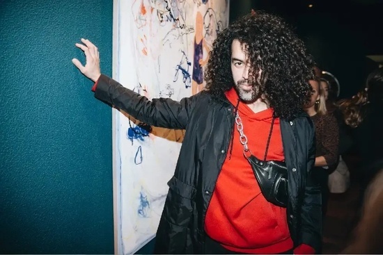 a man with curly hair is standing in front of a painting